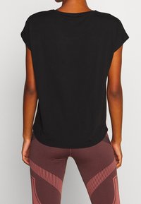 Top corto negro de manga corta con escote redondo, textura suave y corte relajado, combinado con leggings burdeos estampados con líneas verticales.
