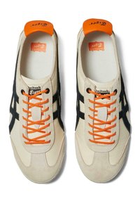 Beżowe buty sportowe z czarnymi akcentami, z pomarańczowymi sznurówkami i językiem. Cholewka ma teksturowane wykończenie i zaokrąglony kształt nosa.