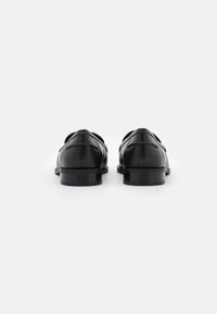 Chaussures en cuir noir avec une finition lisse, à bouts ronds et au design minimaliste. Présentent des coutures discrètes et un talon bas empilé.