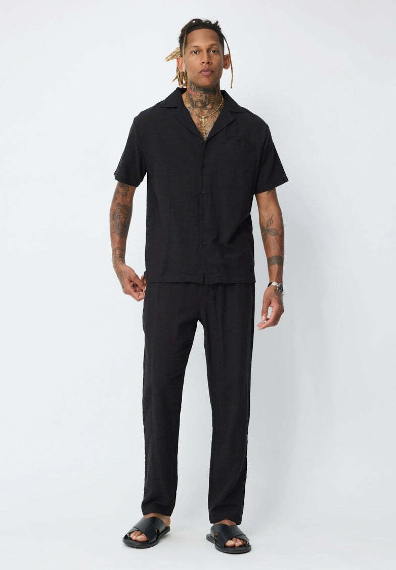 Chemise noire en lin à manches courtes avec col, accompagnée d'un pantalon ample assorti. Tissu léger, texture lisse et design simple.