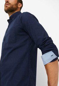 Marineblaues Hemd mit Knopfleiste aus strukturiertem Stoff, das über eine Brusttasche und kontrastierende hellblaue Ärmelbündchen verfügt.