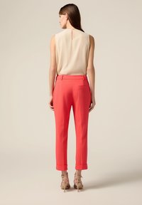 Dames mouwloze beige top met een sleutelgat aan de achterkant, gecombineerd met op maat gemaakte koraalkleurige broek met opgerolde manchetten en een enkele achterzak.