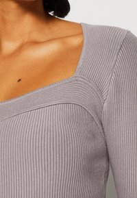 Grau gerippter Oberteil mit quadratischem Ausschnitt, ausgestattet mit einem strukturierten Stoff und einem taillierten Design, das die Schultern und den Ausschnitt betont.