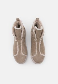 Bottes poignées en suede beige avec une finition texturée, dotées d'une doublure en fourrure apparente et de zips sur les côtés pour un enfilage facile. Bout arrondi et col rembourré.