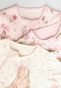 Tre barntröjor med varierade mönster: rosa blommönster, rosa ränder och krämfärgad med en kaninillustration och volanger.