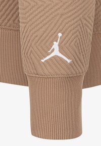 Il tessuto della felpa marrone a coste presenta un motivo a zigzag testurizzato con un logo Jumpman bianco sul polsino della manica destra.