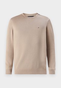 Beige kötött pulóver hosszú ujjakkal, kerek nyakkivágással, bordázott mandzsettákkal és aljjal, amelyen egy kis logós címke található a mellkason.