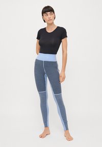 Högmidjade leggings med en blandning av vertikala ränder och geometriska mönster i blå nyanser, tillverkade av stretchigt tyg. Svart åtsittande tröja.
