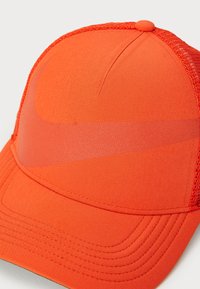 Casquette orange avec un devant en tissu structuré, des côtés en mesh et un visière incurvée. Présente un motif de logo subtil sur le panneau avant.