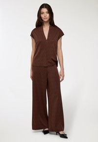 Top marrone con motivo e scollatura a V profonda, maniche corte, abbinato a pantaloni a gamba larga. Entrambi realizzati in materiale morbido, con un sottile design geometrico.