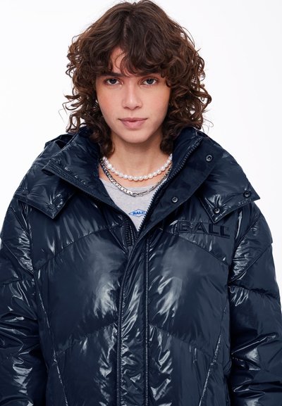 Mornarska puffer jakna z sijočo površino, ki ima zadrgo, snežno gumbe in vezeno logotip. Kapuca je pritrjena in ima prešito vzorec.