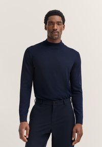 Navyfarbener Rollkragenpullover aus weichem Material, figurbetonte Silhouette, lange Ärmel, kombiniert mit passenden dunklen Hosen, minimalistisches Design.