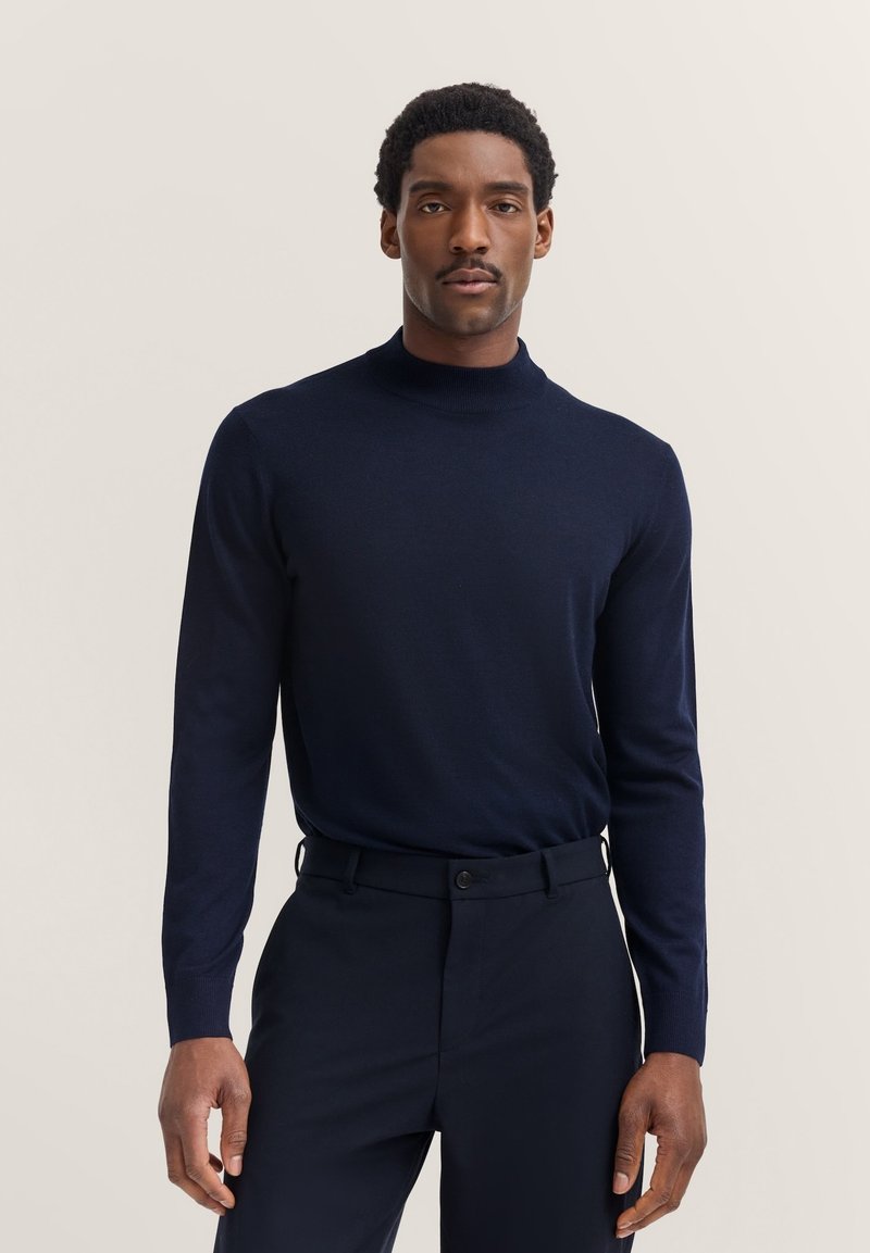 Navyfarbener Rollkragenpullover aus weichem Material, figurbetonte Silhouette, lange Ärmel, kombiniert mit passenden dunklen Hosen, minimalistisches Design.