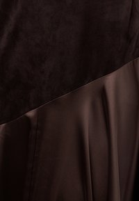 Σκούρο καφέ ύφασμα με υφή σουέτ στην κορυφή και ομαλό σατέν ύφασμα από κάτω, ενωμένα με μια διαγώνια ραφή.