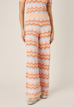 Pantalones de pata ancha con rayas onduladas en rosa, naranja y azul, combinados con una blusa a juego y zapatillas de ballet plateadas.