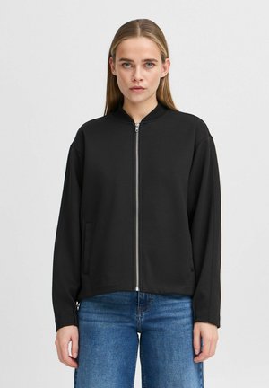 Veste noire à fermeture éclair avec col montant, en tissu lisse, dotée de poches latérales et d'une coupe décontractée. Manches longues, design minimaliste.
