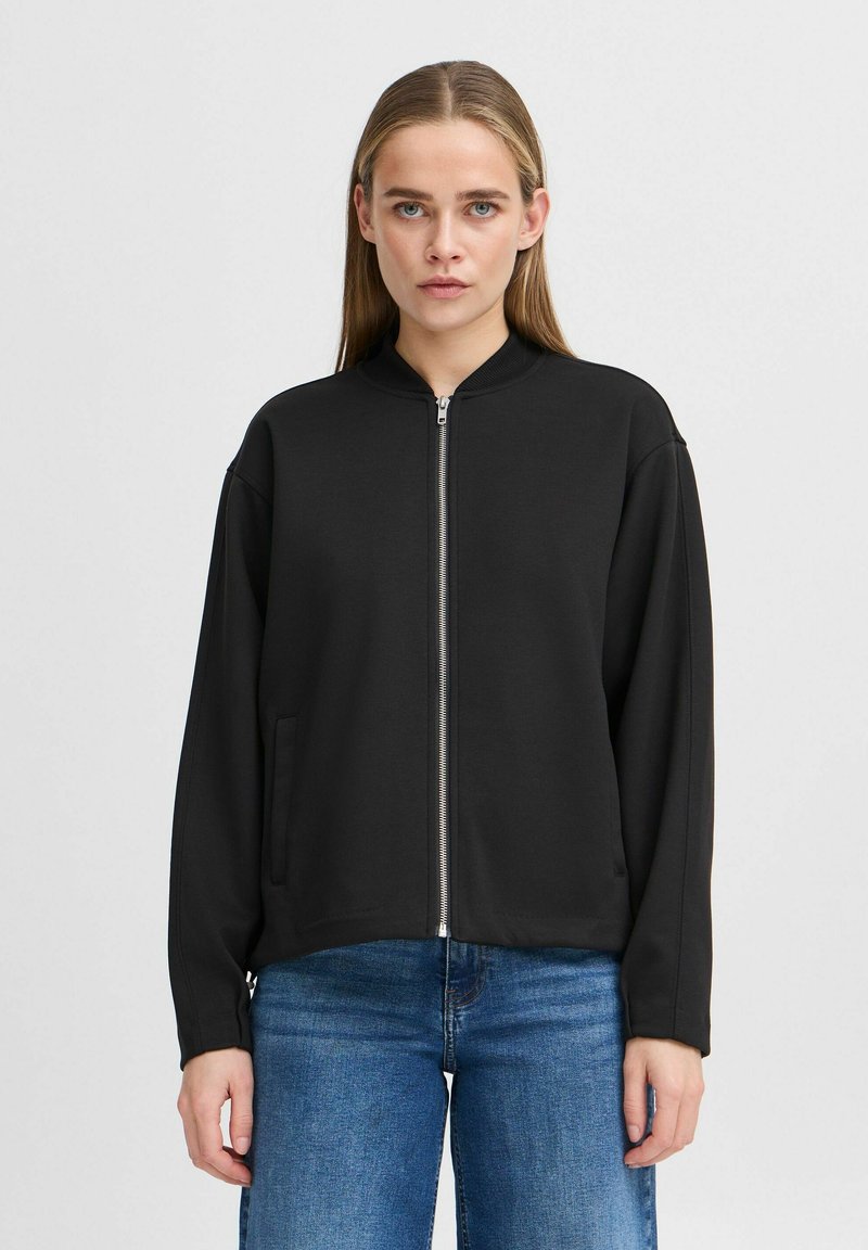 Svart zip-up jacka med ståkrage, gjord av ett smidigt tyg, med sidofickor och en avslappnad passform. Långa ärmar, minimalistisk design.