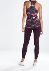 Kolorowy top na ramiączkach z geometrycznymi wzorami, zestawiony z dopasowanymi ciemnoczerwonymi legginsami o subtelnym plamkowanym wzorze oraz białymi trampkami.