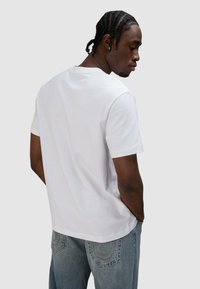 Wit katoenen T-shirt met korte mouwen, ronde hals, losse pasvorm en een gladde textuur. Model getoond van achteren, gedragen met blauwe spijkerbroek.