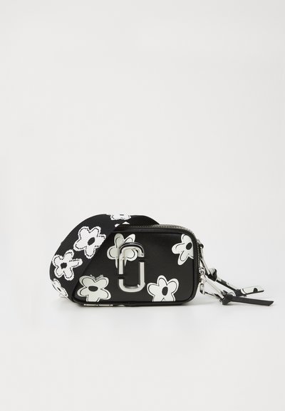 Μαύρη ορθογώνια τσάντα ώμου με λευκό λουλούδι, πλατιά ταιριαστή ιμάντα, κλείσιμο με φερμουάρ και ασημένιο μεταλλικό λογότυπο διπλού J μπροστά.