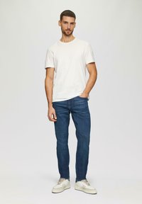 Valkoinen lyhythihainen t-paita, siniset slim-fit farkut ja beigeet tennarit. Yksinkertainen muotoilu, jossa on pyöreä kaula-aukko ja suorat lahkeet.