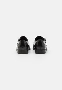Schwarze Lederschuhe mit polierter Oberfläche, mit niedrigem Absatz, abgerundeter Zehenpartie und dekorativen Metallakzenten an beiden Seiten.
