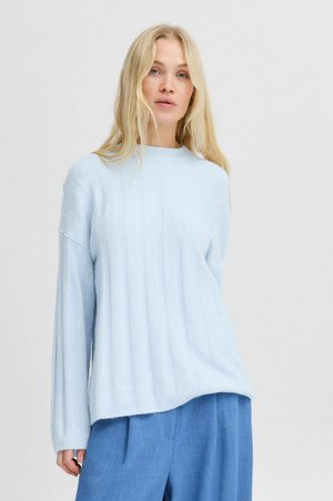 Light blue sweater with a ribbed texture, funnel neck, and dropped shoulders. It has long sleeves and a relaxed fit, paired with blue trousers.