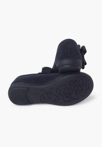 Scarpe in suede blu navy con punta arrotondata, tacco basso e dettaglio decorativo a fiocco sul lato. Suola in gomma testurizzata con un motivo ondulato.