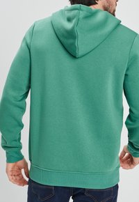 Sudadera con capucha verde hecha de material suave, con un bolsillo tipo canguro y puños de canalé, con un corte relajado y diseño liso.