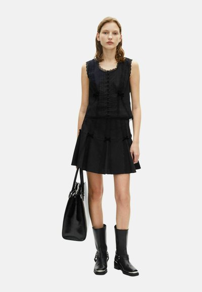 Vestido negro con parte superior sin mangas, detalles de encaje, botonera en el frente y falda en capas. Combinado con botas negras hasta la rodilla y un bolso de hombro.