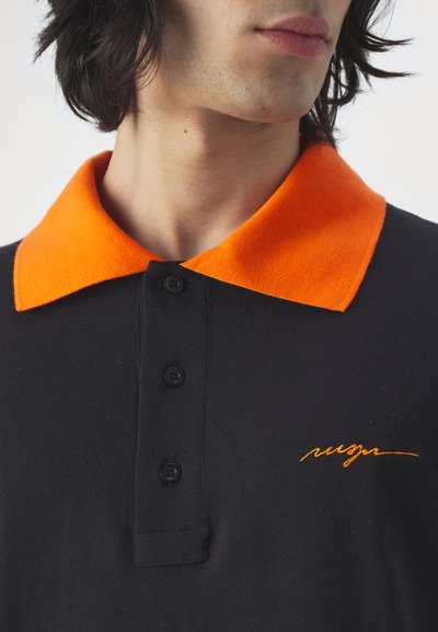 Svart polo-skjorte med en lys orange ullkrage, fire knapper og en subtil, orange brodert logo på brystet.