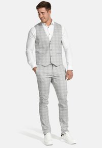 Hellgraue Weste und passende Hose aus strukturiertem Stoff mit dezentem Muster. Getragen mit weißem Hemd und weißen Turnschuhen.