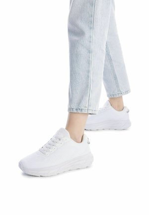 Zapatillas deportivas blancas con parte superior de malla, cordones y suela texturizada. Combinadas con jeans cortos de color azul claro. Diseño simple y moderno.