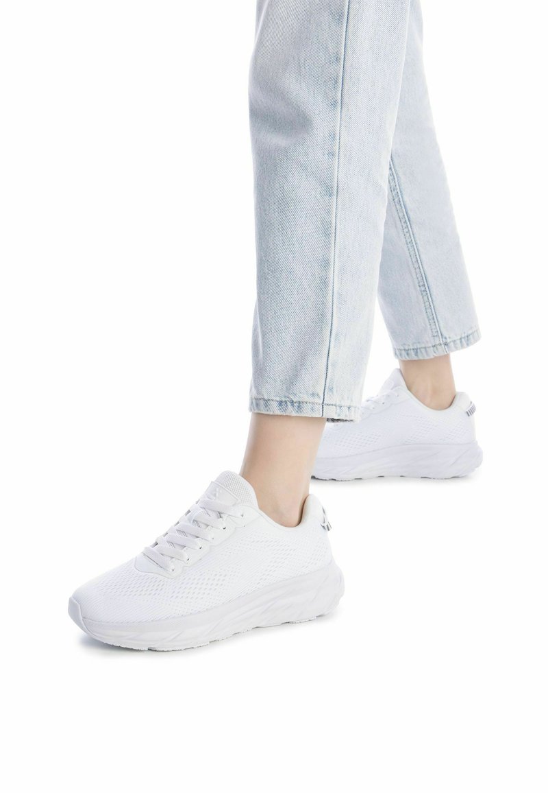 Zapatillas deportivas blancas con parte superior de malla, cordones y suela texturizada. Combinadas con jeans cortos de color azul claro. Diseño simple y moderno.