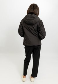 Giacca a vento nera con cappuccio, caratterizzata da un esterno liscio e isolante e una silhouette aderente. Abbinata a pantaloni neri larghi e scarpe bianche.