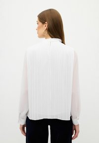 Weiße plissierte Bluse mit einem gerafften Ausschnitt, langen Ärmeln, geknöpften Manschetten und einer transparenten Textur auf der Rückseite.
