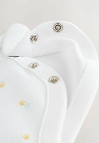 Vit bomullsbody med gula och gröna blomsterbroderier samt silverfärgade tryckknappar längs halsringningen och nederkanten. Texturerad yta.