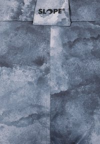 Textiljacka i ett blågrått akvarellmönster, med en slät textur, framträdande sömmar och en logotagg märkt "SLOPE."