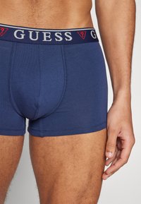 Námorníckomodré bavlnené boxerky s kontrastným elastickým pásom s logom "GUESS" a trojuholníkovým akcentom. Hladká textúra, priliehavý strih.