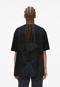 Sort oversized t-shirt med et grafisk print på ryggen, korte ærmer og afslappet pasform. Viser flettet hår set bagfra.