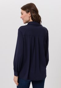 Dunkelblaue Bluse mit langen Ärmeln, weichem Stoff, geknöpften Manschetten und lockerem Schnitt, mit einer Rückenfalte für mehr Bewegungsfreiheit und Komfort.