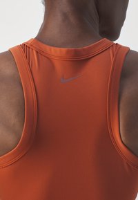 Orangenes sportliches Tanktop mit rundem Ausschnitt und einem dezenten Nike-Logo auf der Rückseite. Der Stoff wirkt glatt und eng anliegend mit verstärkten Nähten.
