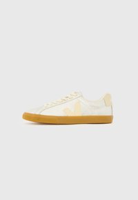 Αθλητικά παπούτσια με επάνω μέρος από λαμπερό ανοιχτόχρυσο, αντίθετο μπεζ λογότυπο και σόλα από καουτσούκ καφέ. Διαθέτουν στρογγυλεμένη μύτη και επίπεδα κορδόνια.