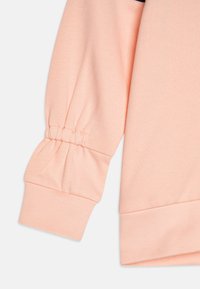 Peach-colored sweatshirt sleeve with gathered cuff detail, ribbed hem, and smooth fabric texture. Suitable for casual wear.