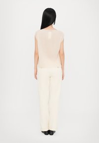 Beige, ribbed top with a slightly loose fit, round neckline, and cap sleeves, paired with cream, straight-leg pants and black shoes.