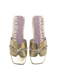 Zapatos de slip-on color oro con tacón plano, que presentan una correa texturizada y un lazo decorativo, con una plantilla morada que muestra "MARIAMA".