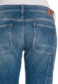 Jean en denim bleu foncé avec une finition délavée, grandes poches arrière et une patch en cuir beige sur la ceinture.