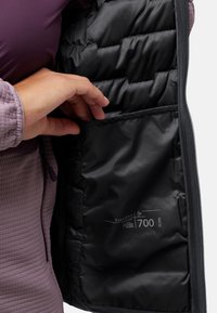 Lila Puffjacke mit einem schwarzen, gesteppten Innenfutter. Verfügt über eine innere Tasche mit der Bezeichnung "Expedry" und Isolationsdetails. Mit Reißverschluss vorne.