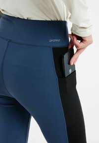 Jūros laivyno ir juodos spalvos leggingai su aukštu juosmeniu, su šonine kišene, kurioje telpa išmanusis telefonas, pagaminti iš tamprios, lygaus audinio.