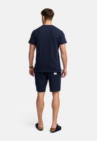 Marineblaues Kurzarmhemd mit einem strukturierten Muster, kombiniert mit passenden Shorts. Einfaches Design mit einem Rückenschild und lässigem Schnitt.
